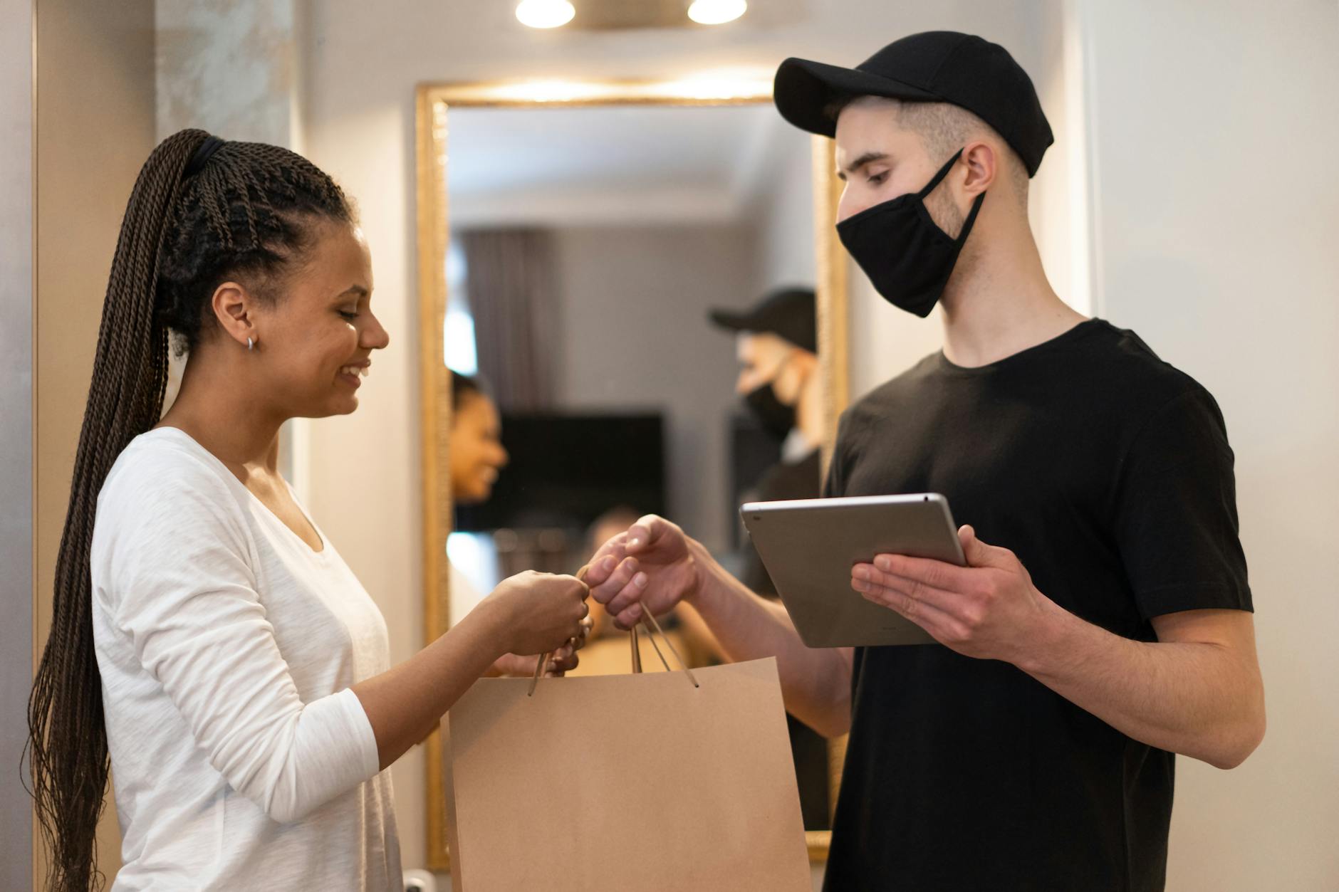 a man wearing face mask handing over a shopping bag to the woman in white long sleeves